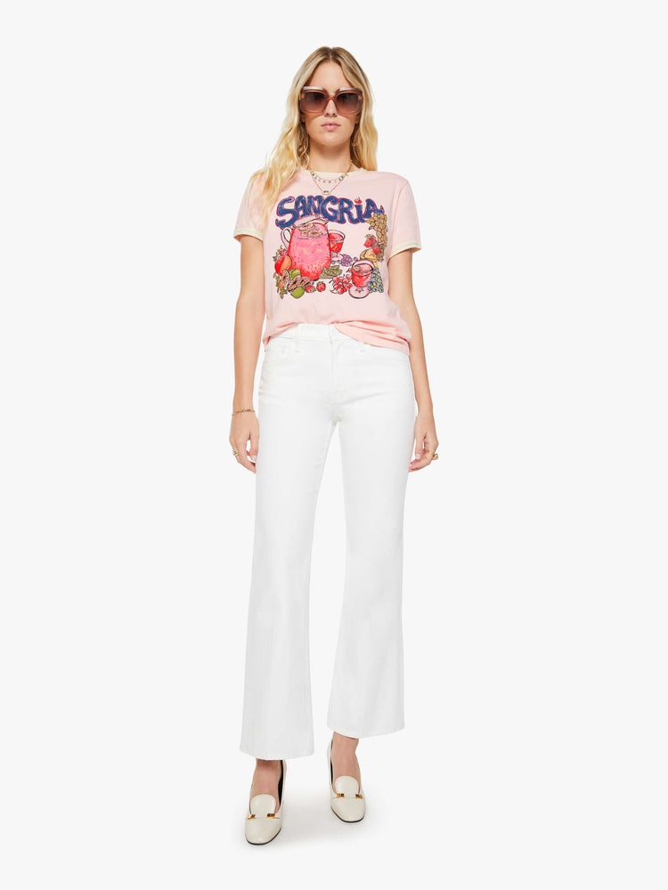 Full body view of a woman in a light pink with cream trim tee with extra-short sleeves and a slightly shrunken fit.