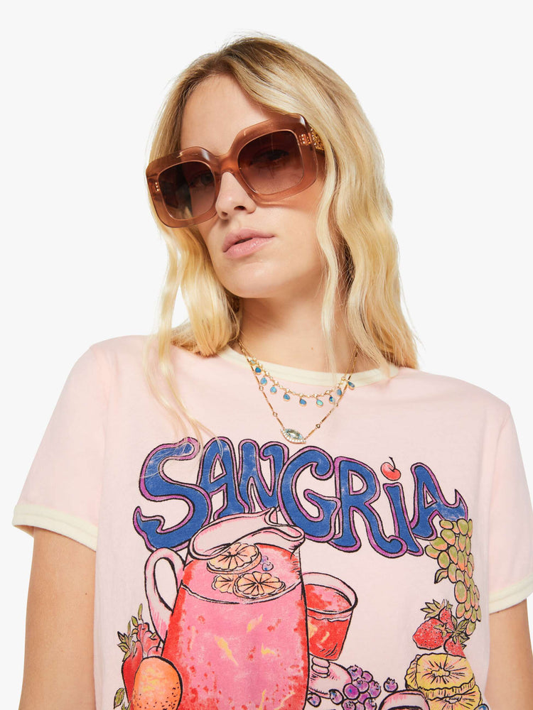 Close up view of a woman in a light pink with cream trim tee with extra-short sleeves and a slightly shrunken fit.