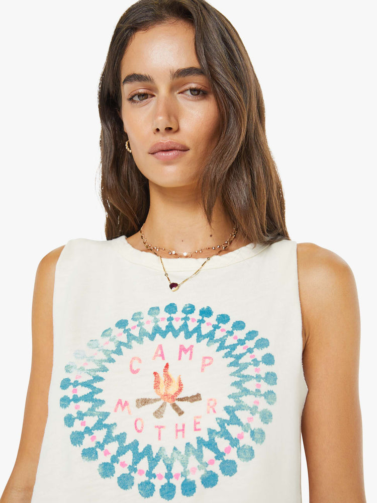 Close up view of a woman in an off-white top features a campfire graphic with text in pink on the front cut off sleeveless top.