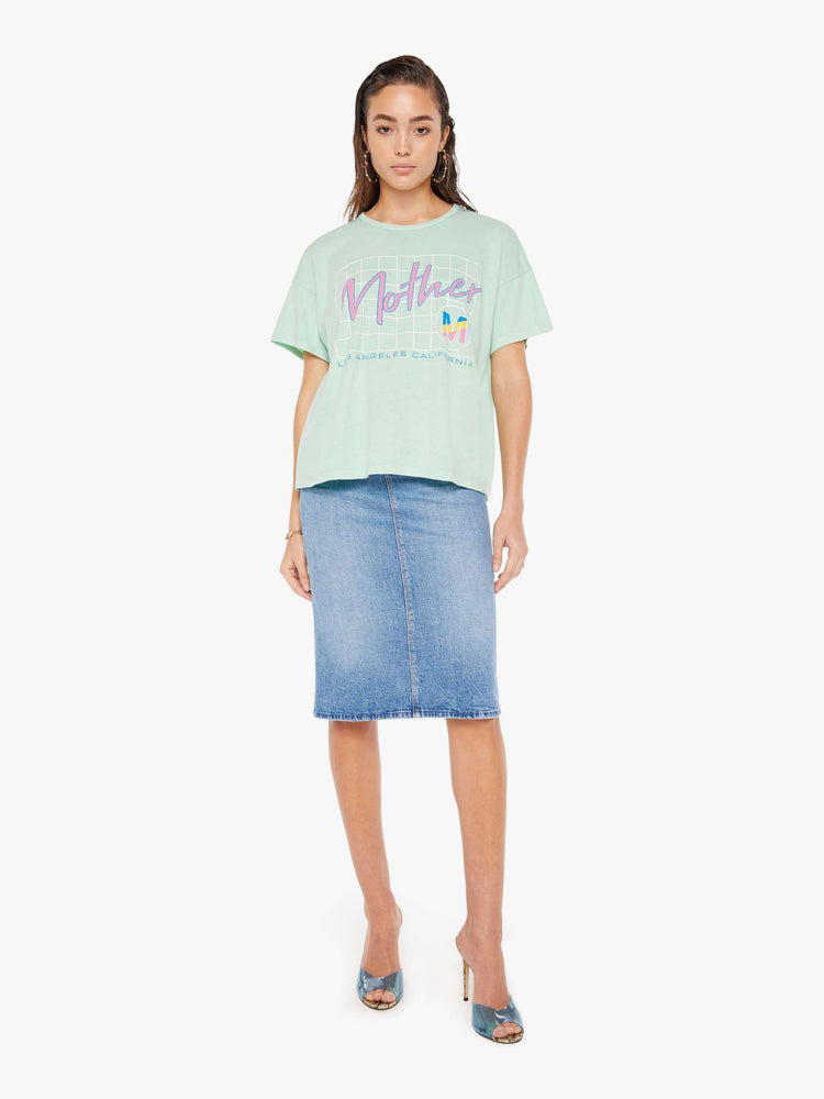 Front full body view of a woman wearing a light teal crew neck tee with an oversized fit, featuring a retro inspired graphic that reads "Mother", paired with a medium blue wash denim skirt.