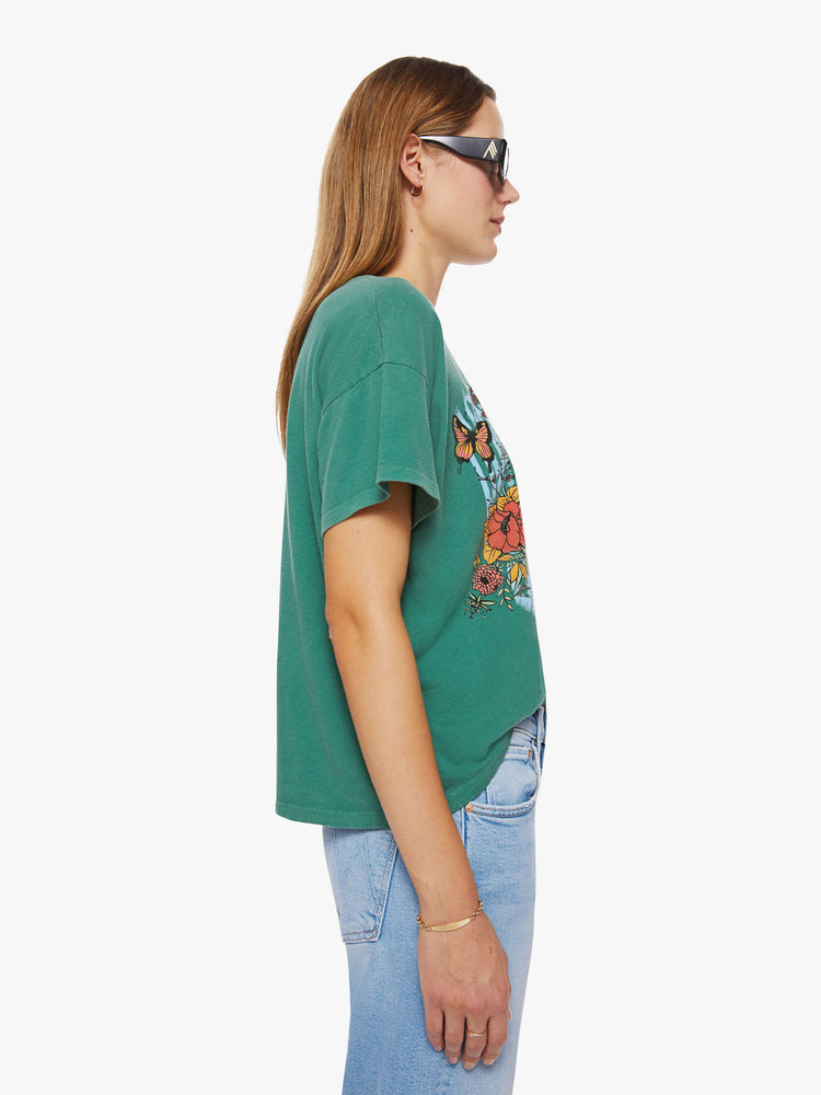Side view of a woman oversize tee with drop shoulders and a loose, boxy fit in a washed green hue with trippy graphic text and flowers.