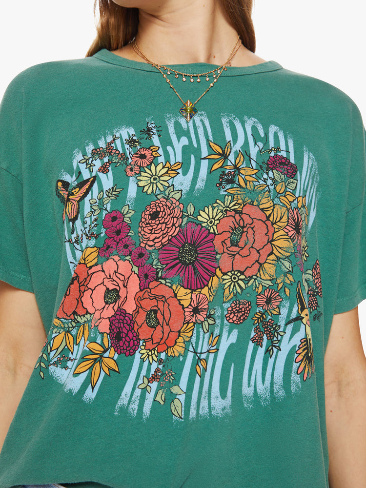 Close up view of a woman oversize tee with drop shoulders and a loose, boxy fit in a washed green hue with trippy graphic text and flowers.