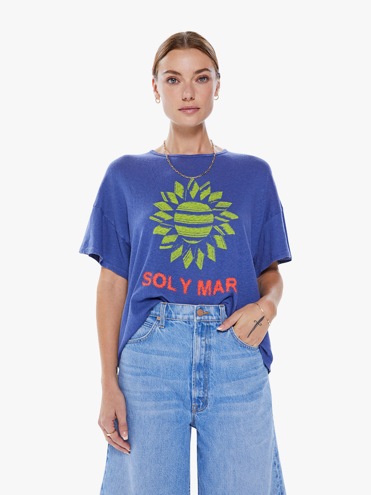 Front view of a women's blue oversized  tee with drop shoulders and a loose, boxy fit with a green sun graphic and text in red.