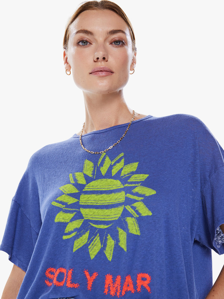 Close up view of a women's blue oversized tee with drop shoulders and a loose, boxy fit with a green sun graphic and text in red.