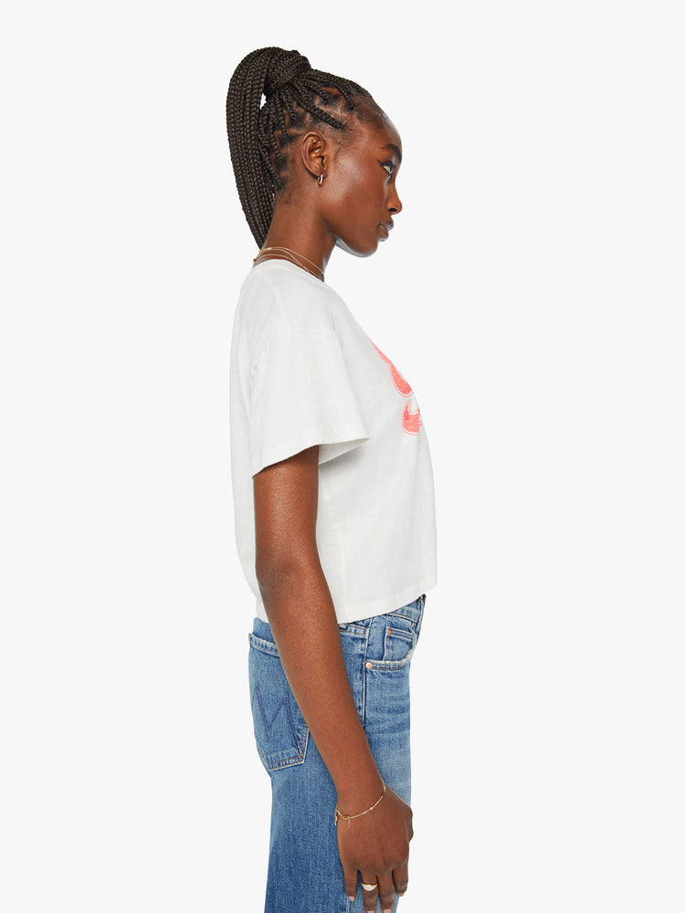 Side view of a woman oversized crewneck tee with a cropped hem in an off white with a peach graphic in front.
