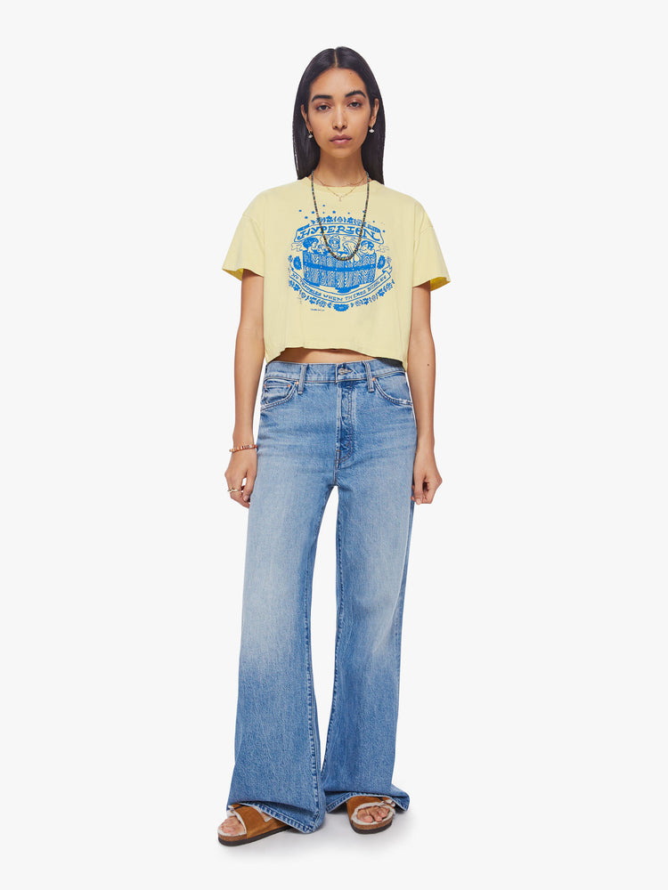 Full body view of a woman cropped tee with a ribbed crewneck, drop shoulders and a boxy fit in a pale yellow hue with a blue graphic in front.