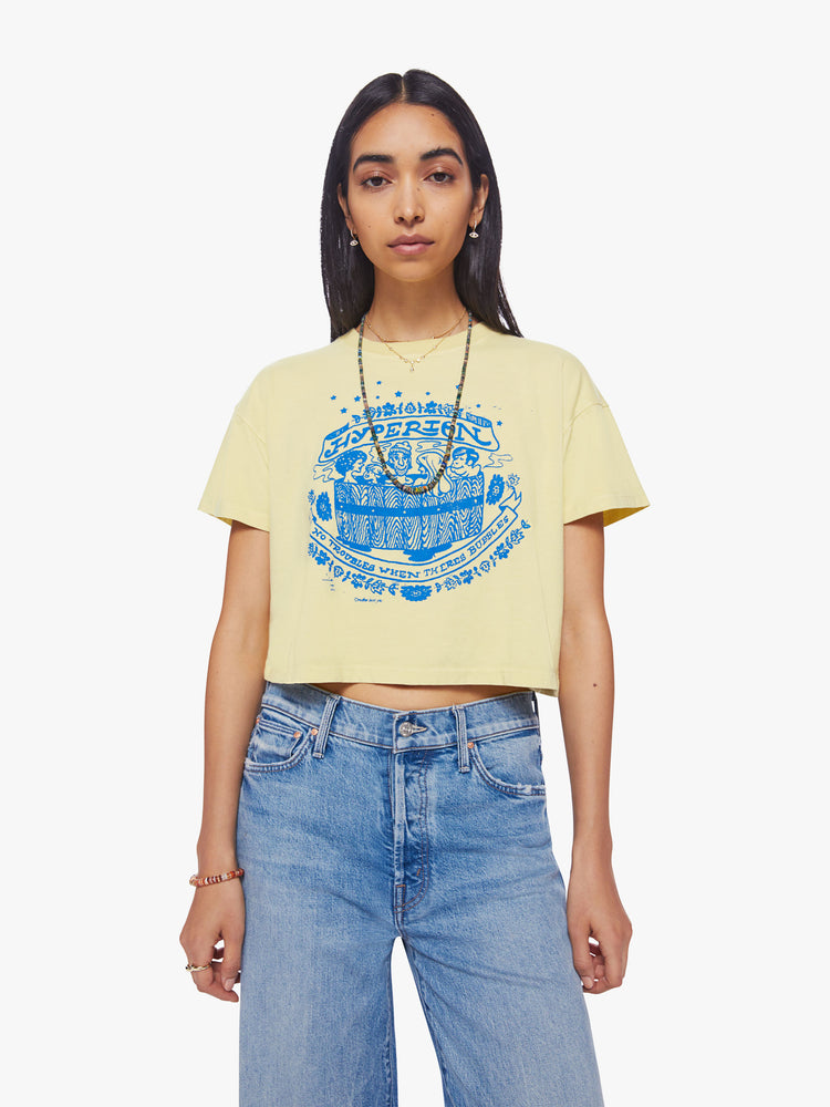 Front view of a woman cropped tee with a ribbed crewneck, drop shoulders and a boxy fit in a pale yellow hue with a blue graphic in front.
