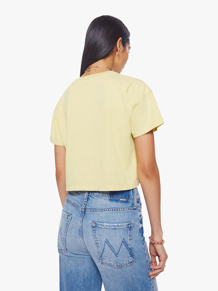 Back view of a woman cropped tee with a ribbed crewneck, drop shoulders and a boxy fit in a pale yellow hue with a blue graphic in front.