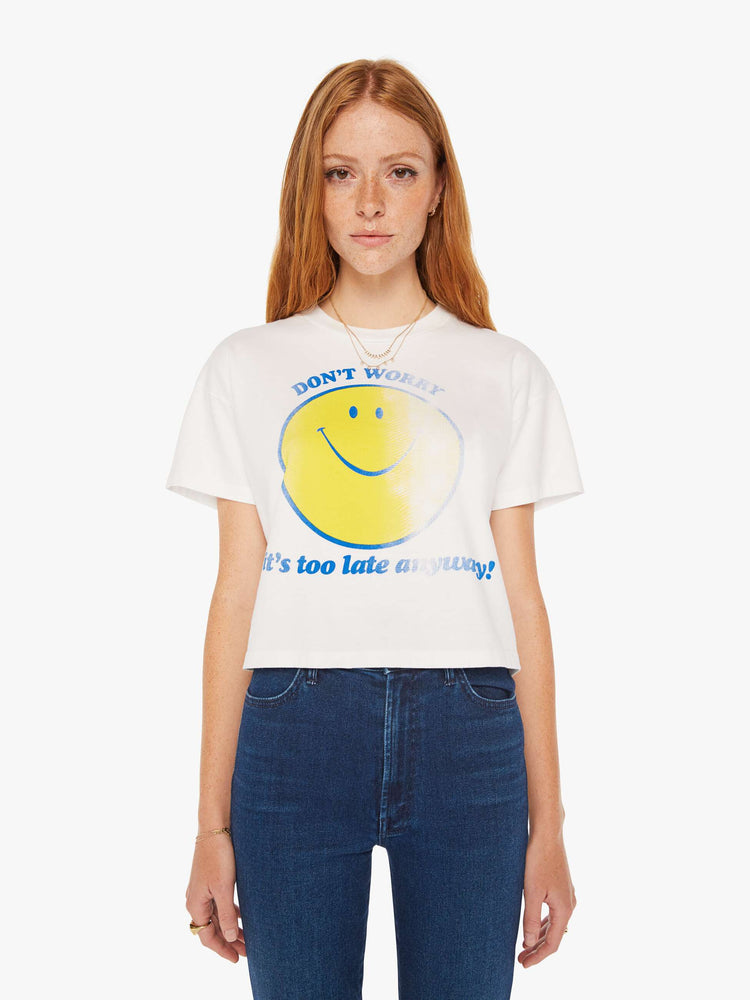 Front view of a women white oversized crewneck tee with drop shoulders, a cropped hem and a boxy fit with a faded smiley graphic with text in blue on the front.