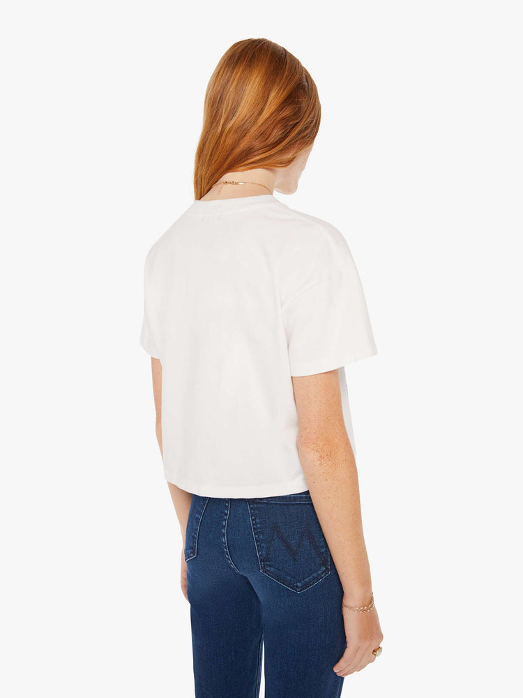 Back view of a women white oversized crewneck tee with drop shoulders, a cropped hem and a boxy fit with a faded smiley graphic with text in blue on the front.
