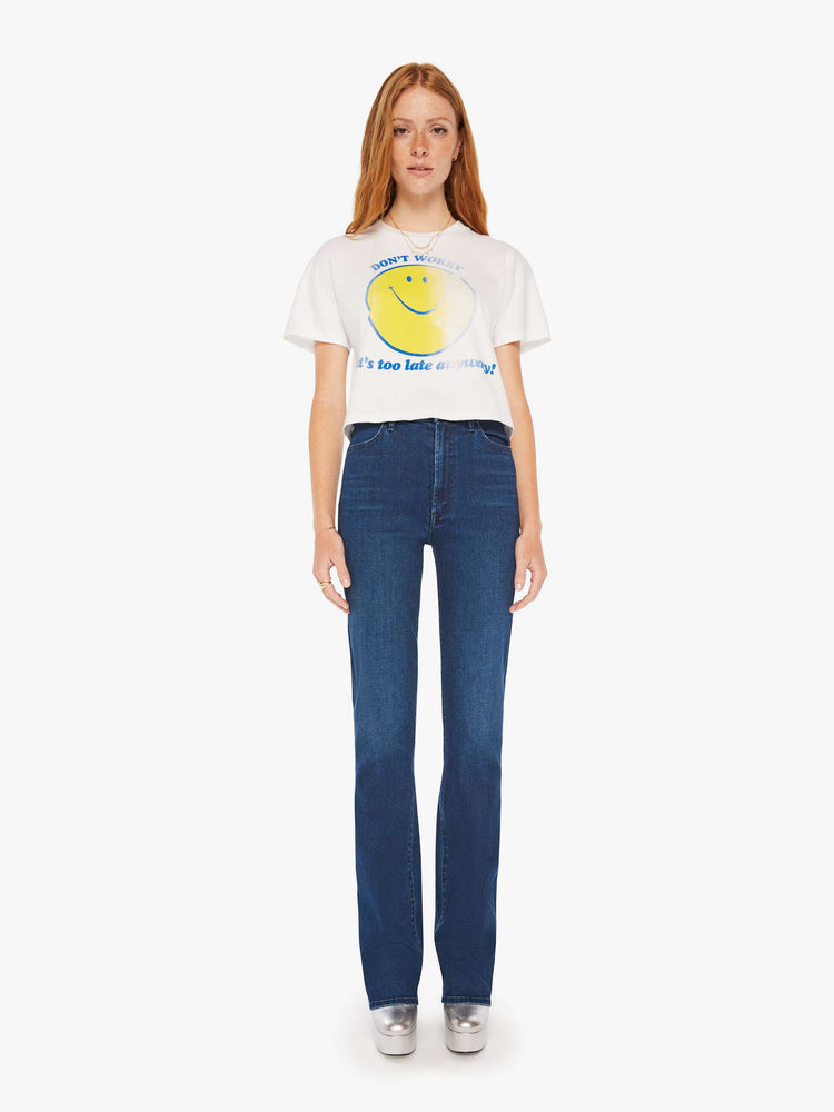 Full body view of a women white oversized crewneck tee with drop shoulders, a cropped hem and a boxy fit with a faded smiley graphic with text in blue on the front.