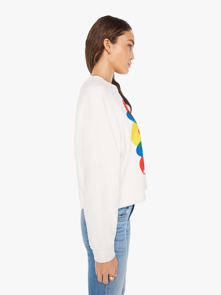 Side view of a woman cropped sweatshirt with a crew neck, drop shoulders and a raw hem in white with an overlapping abstract graphic and text in black on the front.