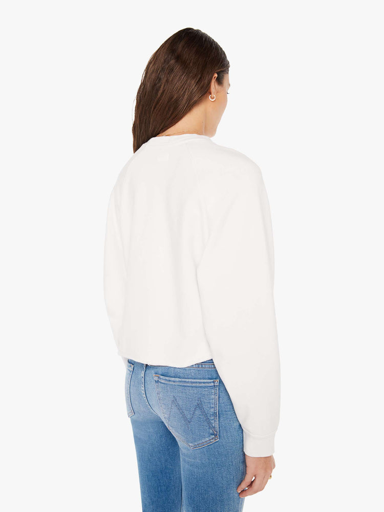 Back view of a woman cropped sweatshirt with a crew neck, drop shoulders and a raw hem in white with an overlapping abstract graphic and text in black on the front.