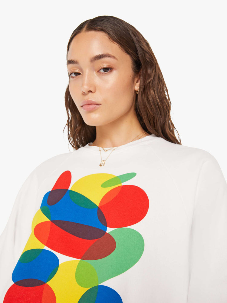Close up view of a woman cropped sweatshirt with a crew neck, drop shoulders and a raw hem in white with an overlapping abstract graphic and text in black on the front.