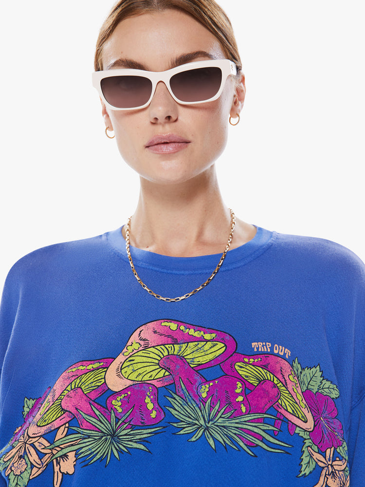 Close up view of a women blue crewneck sweatshirt with dropped sleeves, a relaxed fit and a cropped elastic hem with a neon mushroom graphic and some subtle advice.