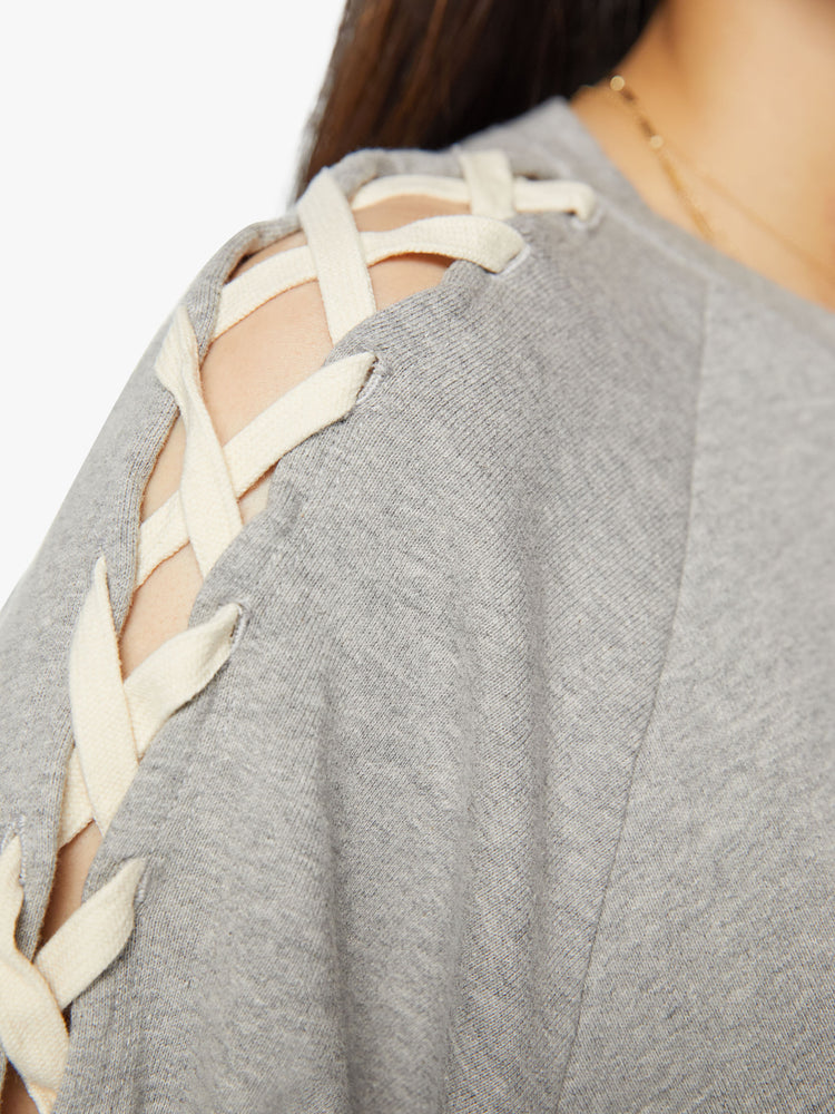 Arm close up view of a woman raglan sweatshirt with thick hems and a slightly boxy fit in grey with laced slide details in cream down the arm.