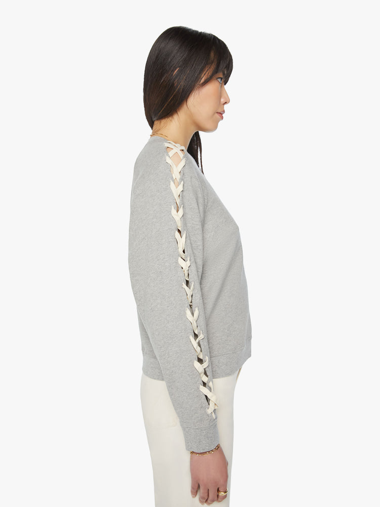Side view of a woman raglan sweatshirt with thick hems and a slightly boxy fit in grey with laced slide details in cream down the arm.