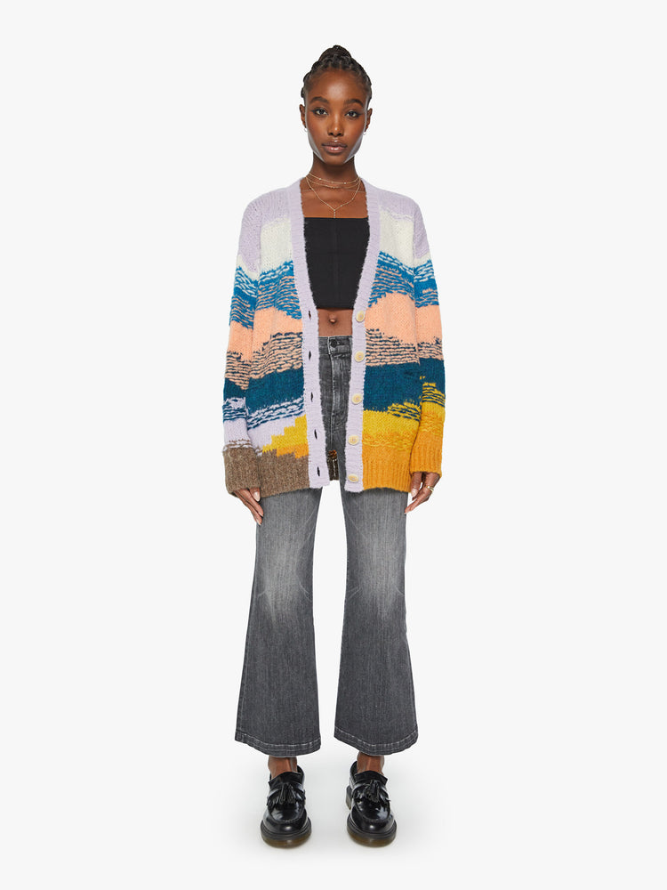 Full body view of a woman oversized cardigan with a V-neck, drop shoulders, buttons down the front and ribbed hems in shades of orange, navy, lavender and blue, and is designed with reverse stitching for texture.
