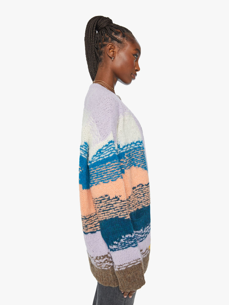 Side view of a woman oversized cardigan with a V-neck, drop shoulders, buttons down the front and ribbed hems in shades of orange, navy, lavender and blue, and is designed with reverse stitching for texture.
