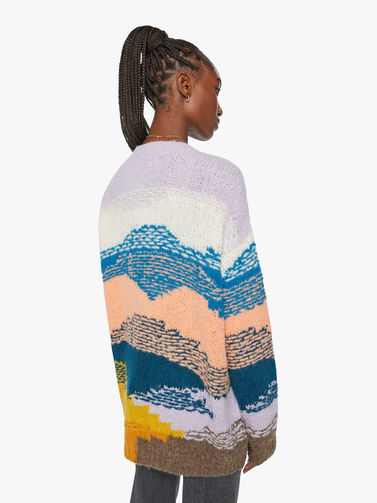 Back view of a woman oversized cardigan with a V-neck, drop shoulders, buttons down the front and ribbed hems in shades of orange, navy, lavender and blue, and is designed with reverse stitching for texture.