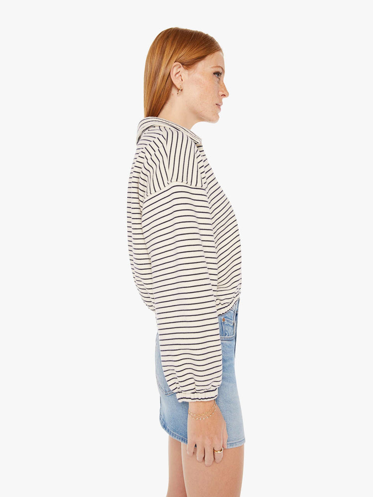 Side view of a womens black and white striped pullover featuring an opened collar and a cropped, cinched waist.