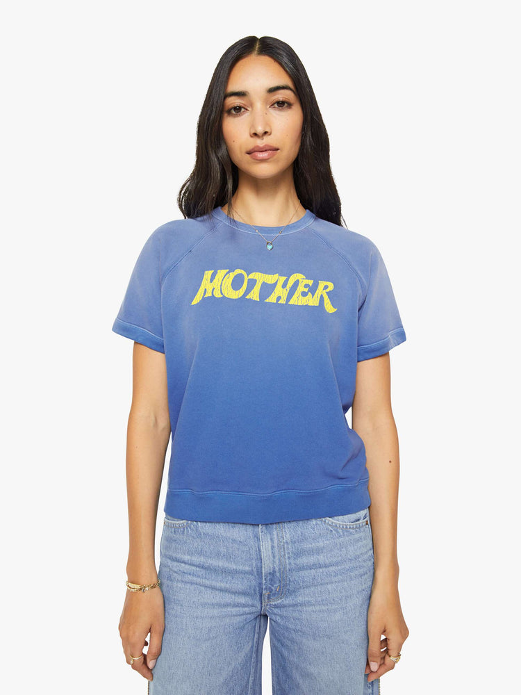 Front view of a woman in a blue with fading across the chest and shoulders and MOTHER's name in crackle-printed yellow text on the front short sleeve sweatshirt.