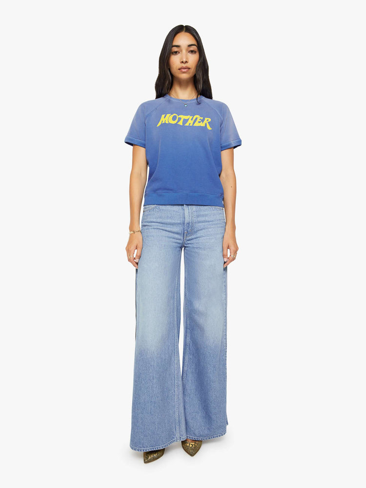 Full body view of a woman in a blue with fading across the chest and shoulders and MOTHER's name in crackle-printed yellow text on the front short sleeve sweatshirt.