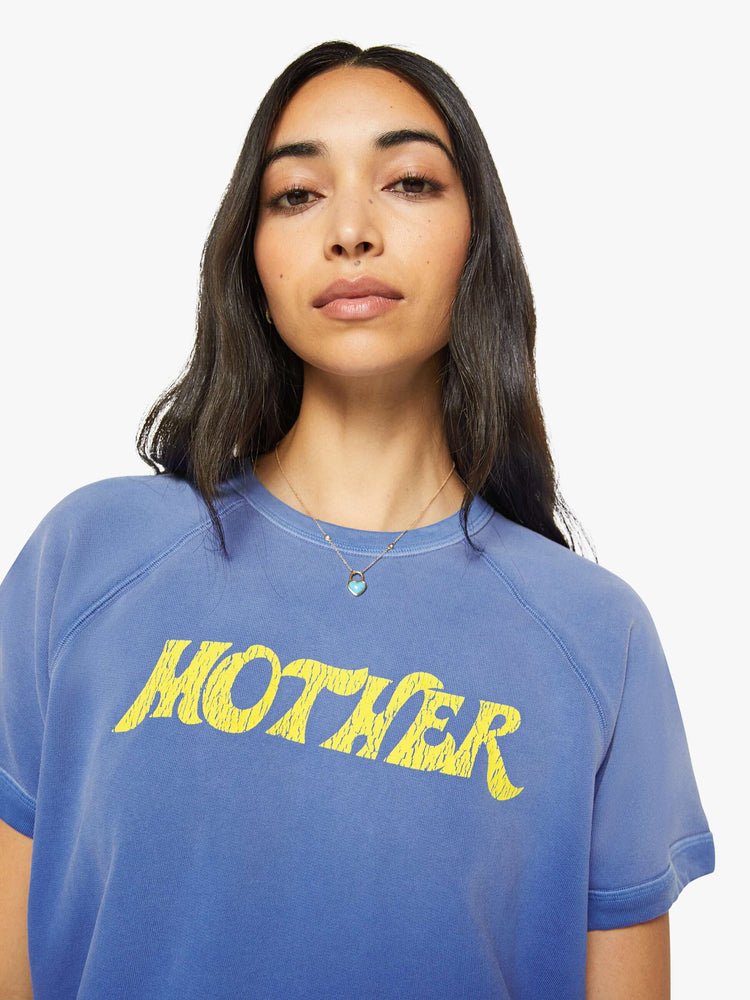 Close up view of a woman in a blue with fading across the chest and shoulders and MOTHER's name in crackle-printed yellow text on the front short sleeve sweatshirt.