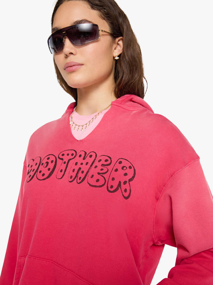 Close up view of a woman in a hoodie is designed in hot pink with sun fading across the shoulders and MOTHER's name in faded black text on the front.