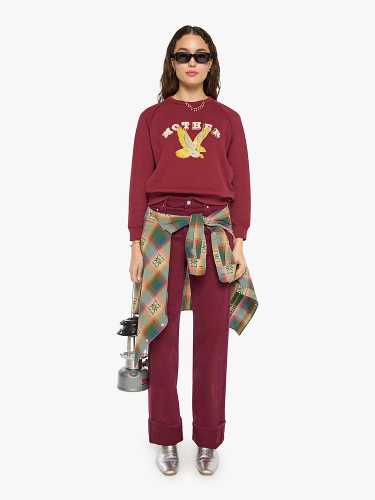 Full body view of a woman in a maroon with MOTHER's name in cream and a pastel eagle graphic in fuzzy puff print sweater.
