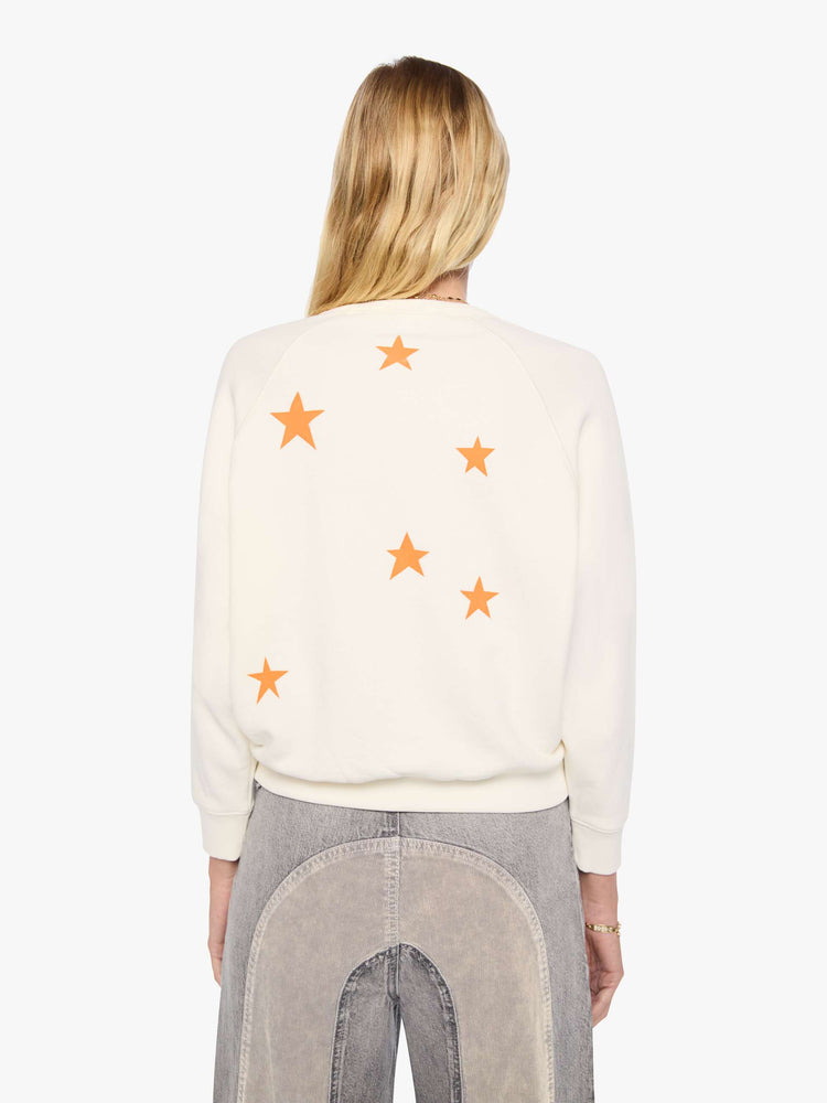 Back view of a woman in off-white with MOTHER's name in blue block text across the chest, studded details and golden yellow stars on the back sweatshirt.