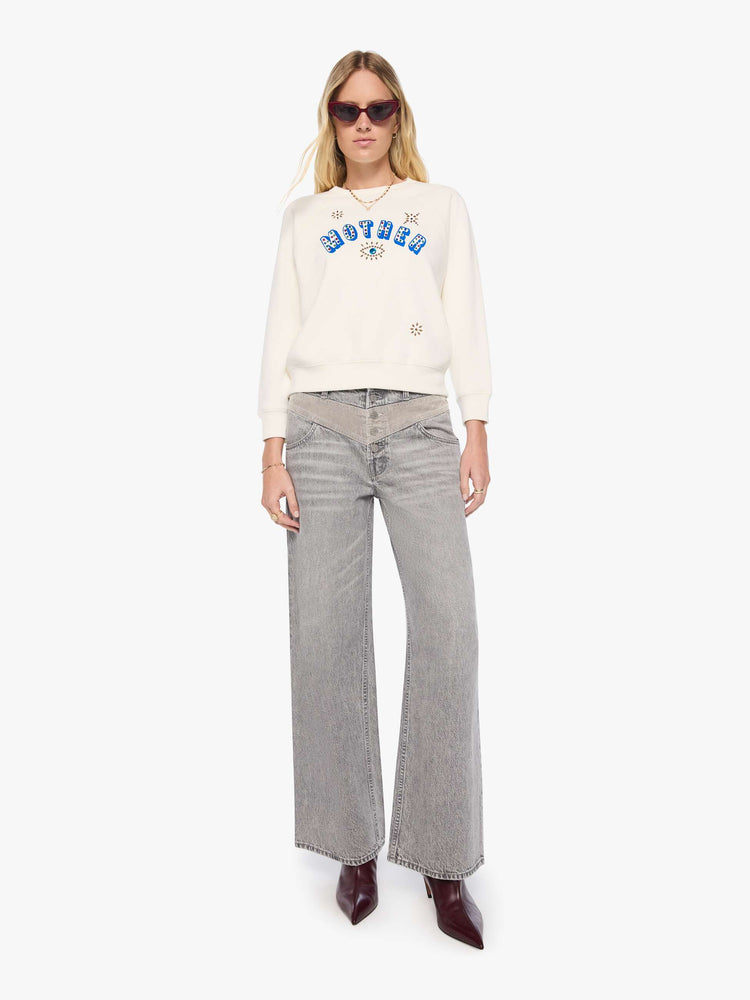 Full body view of a woman in off-white with MOTHER's name in blue block text across the chest, studded details and golden yellow stars on the back sweatshirt.