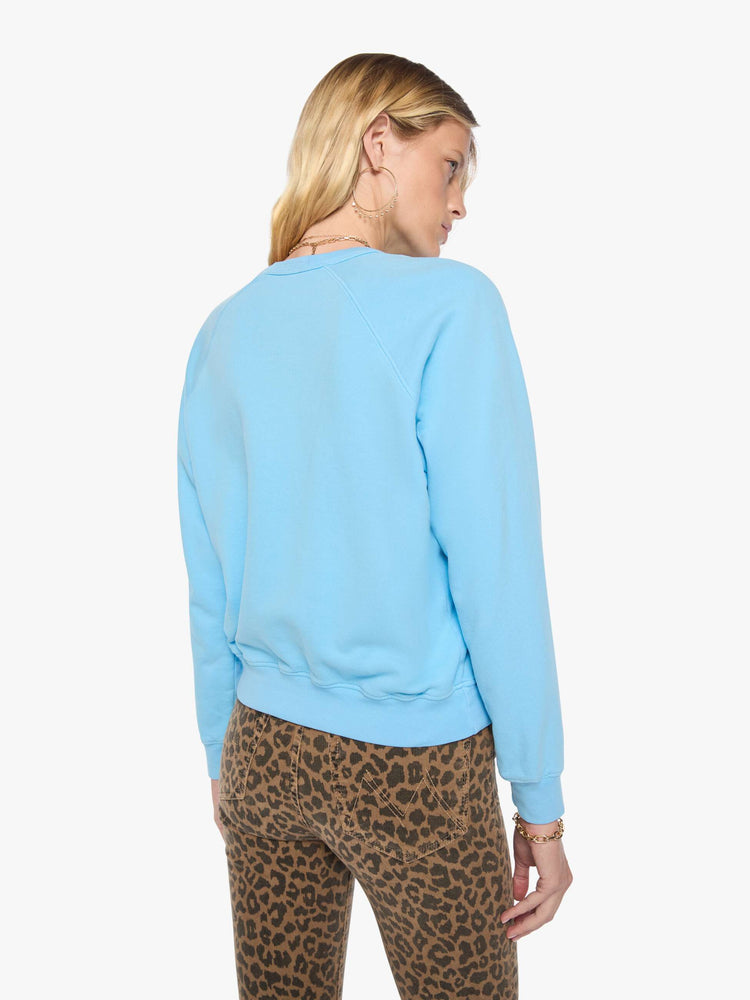 Back view of a woman in a light blue sweatshirt features a faded text graphic in red across the front.