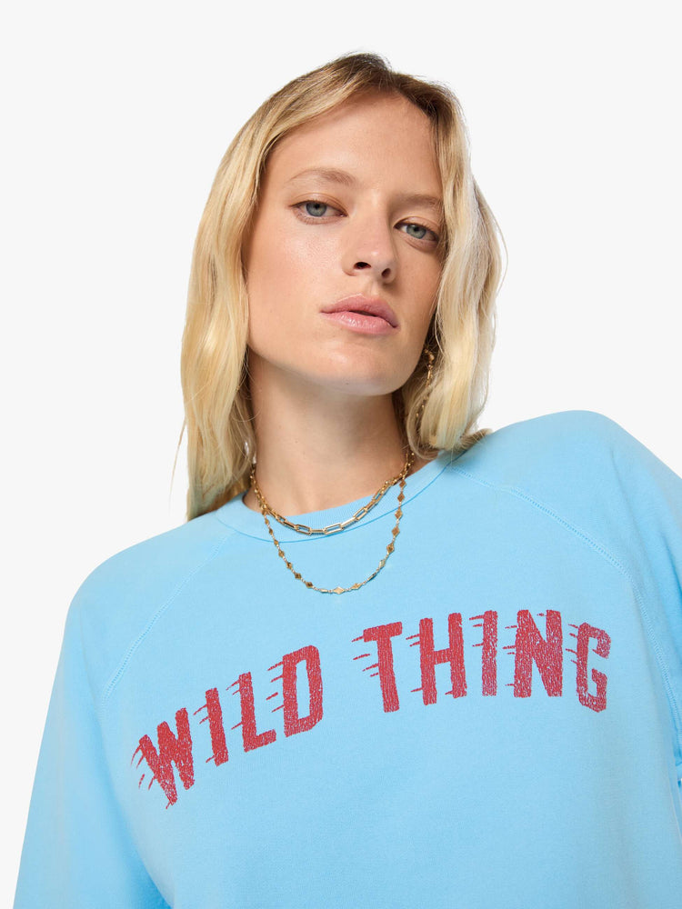 Close up view of a woman in a light blue sweatshirt features a faded text graphic in red across the front.