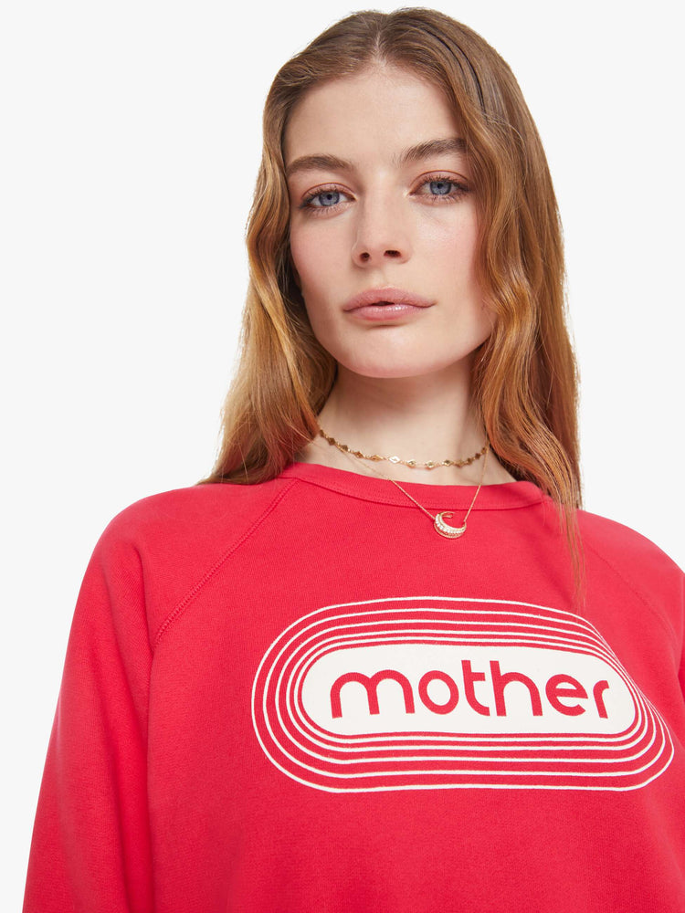 Close up view in a woman in a crewneck sweatshirt in red with a white text graphic and MOTHER's name on the front.