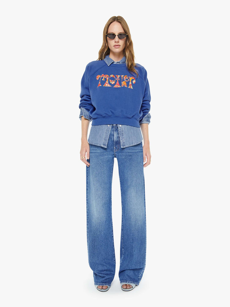 Full body view of a woman in blue with  a floral block letters sweatshirt with a crewneck, ribbed hems and a slightly cropped fit.