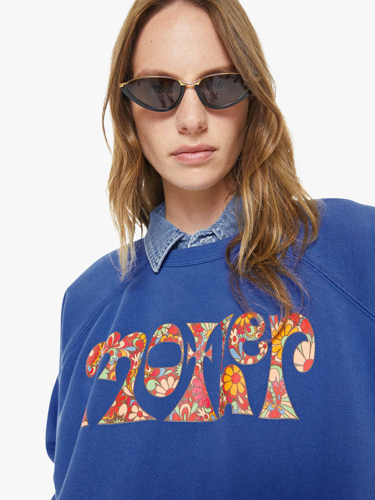 Close up view of a woman in blue with  a floral block letters sweatshirt with a crewneck, ribbed hems and a slightly cropped fit.