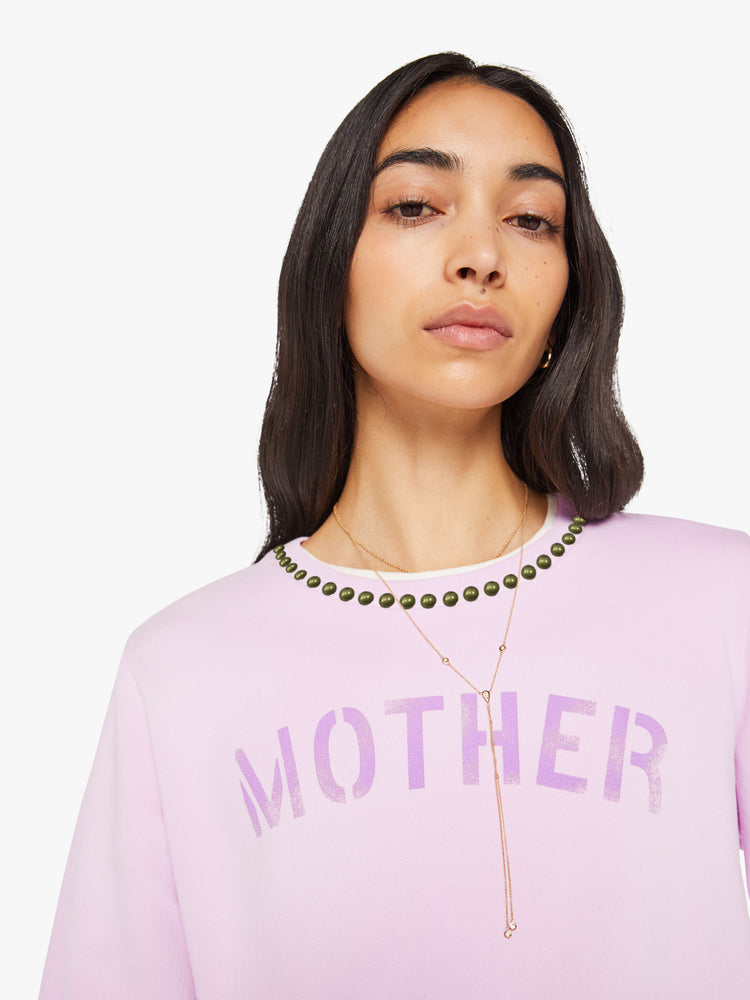 Close up view of a woman in a pale orchid sweatshirt with studs along the neckline and MOTHER's name stenciled in purple across the front.