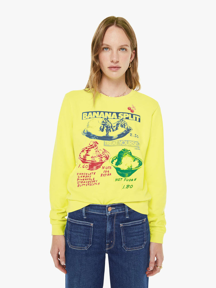 Front view of a woman in a bright yellow sweatshirt with a banana split graphic in blue, red and green on the front.