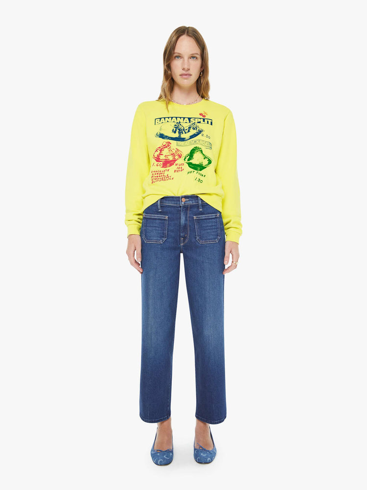 Full body view of a woman in a bright yellow sweatshirt with a banana split graphic in blue, red and green on the front.
