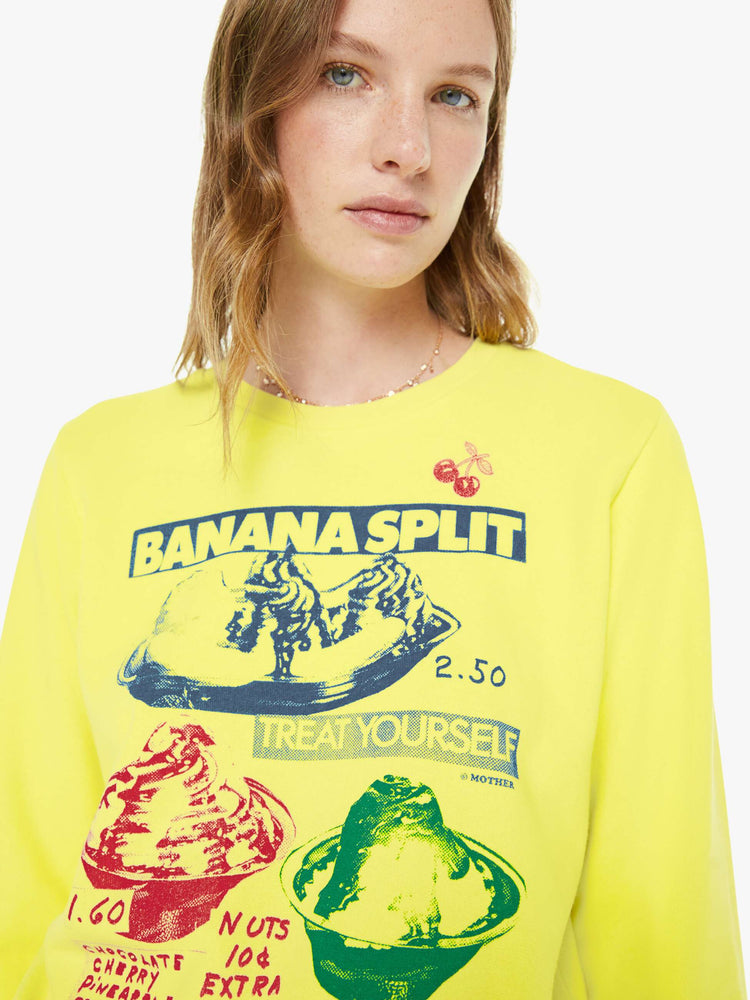 Close up view of a woman in a bright yellow sweatshirt with a banana split graphic in blue, red and green on the front.