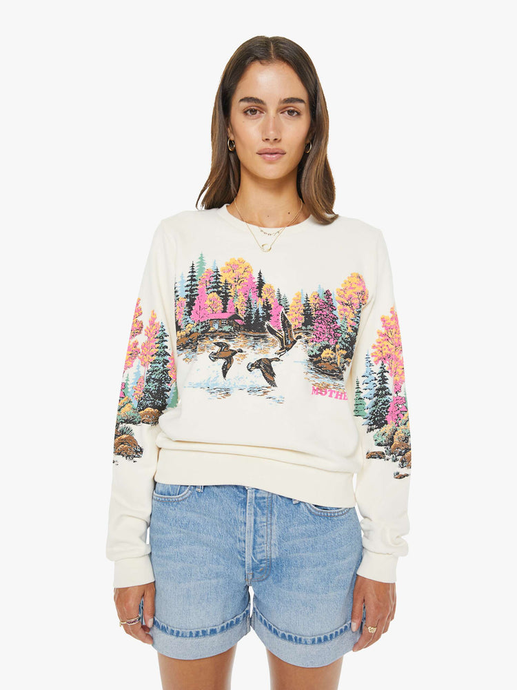 Front view of a woman in an off white sweatshirt features an idyllic lakeside graphic with MOTHER's name in pink on the front.