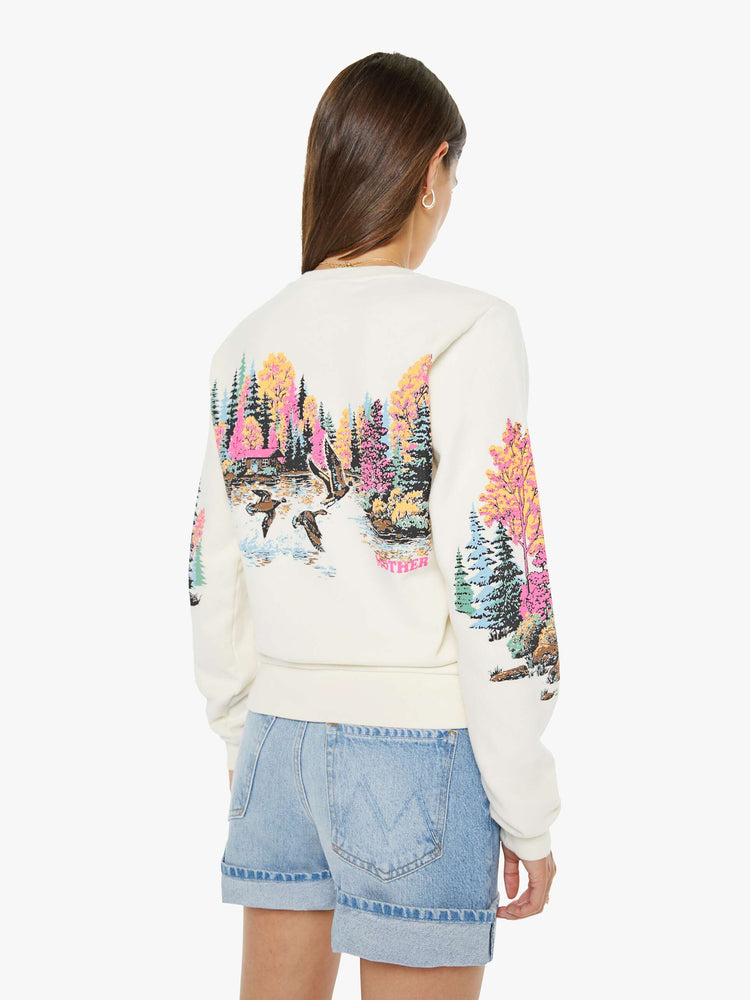 Back view of a woman in an off white sweatshirt features an idyllic lakeside graphic with MOTHER's name in pink on the front.