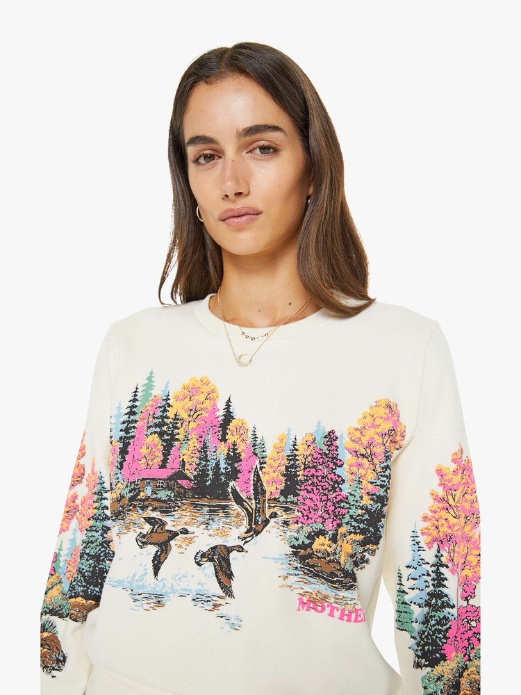 Front close up view of a woman in an off white sweatshirt features an idyllic lakeside graphic with MOTHER's name in pink on the front.