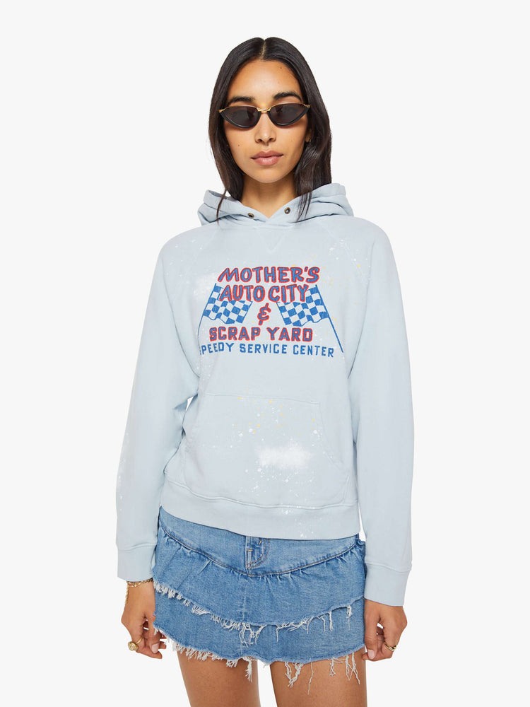 Front view of a woman in a light blue, the hoodie features a crackle-printed scrap yard graphic on the front with paint and bleach splatters throughout.