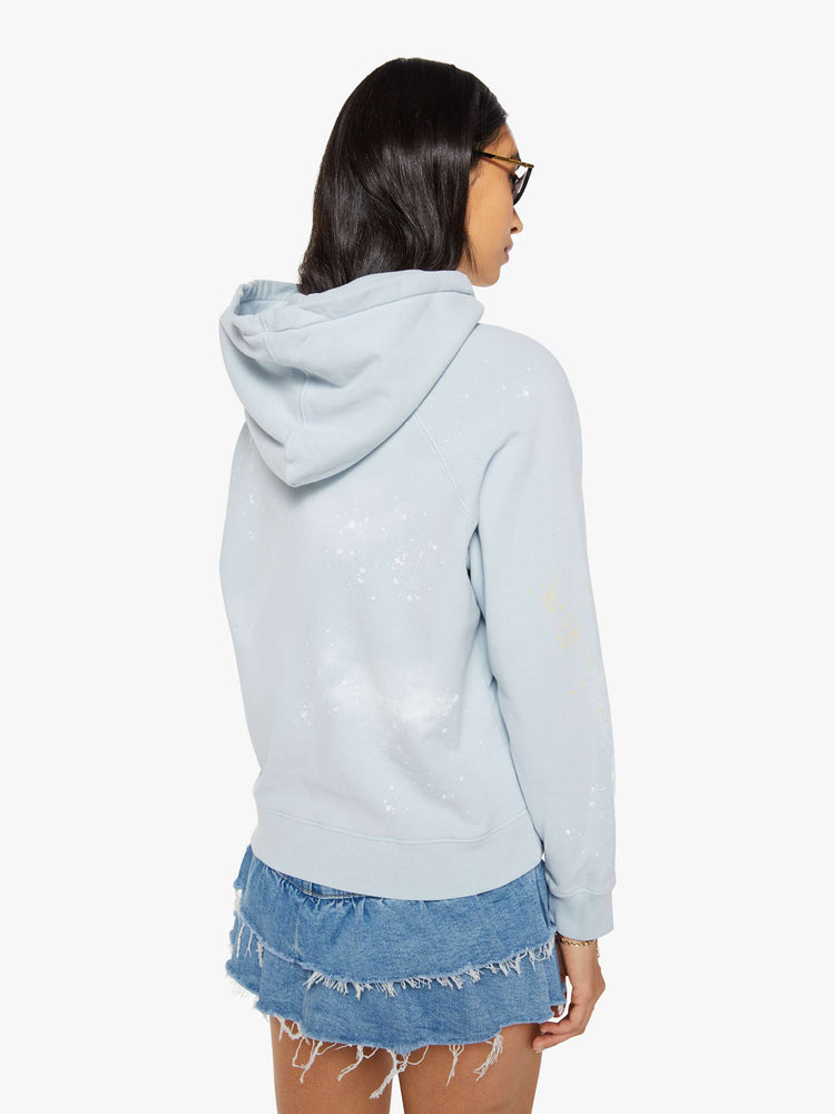 Back view of a woman in a light blue, the hoodie features a crackle-printed scrap yard graphic on the front with paint and bleach splatters throughout.