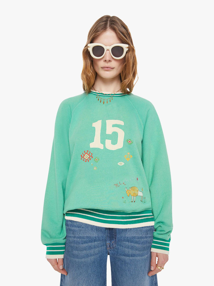 Front view of a woman in a sun-faded green sweatshirt with colorful embroidery throughout and the number 15 appliqued on the front.