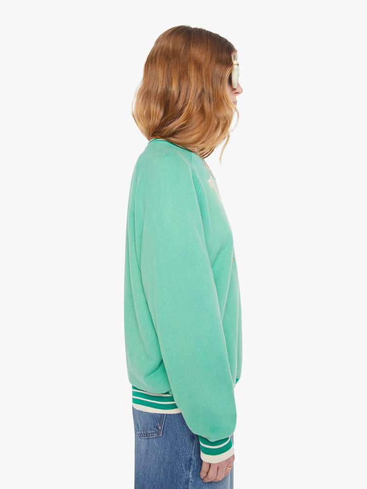 Side view of a woman in a sun-faded green sweatshirt with colorful embroidery throughout and the number 15 appliqued on the front.