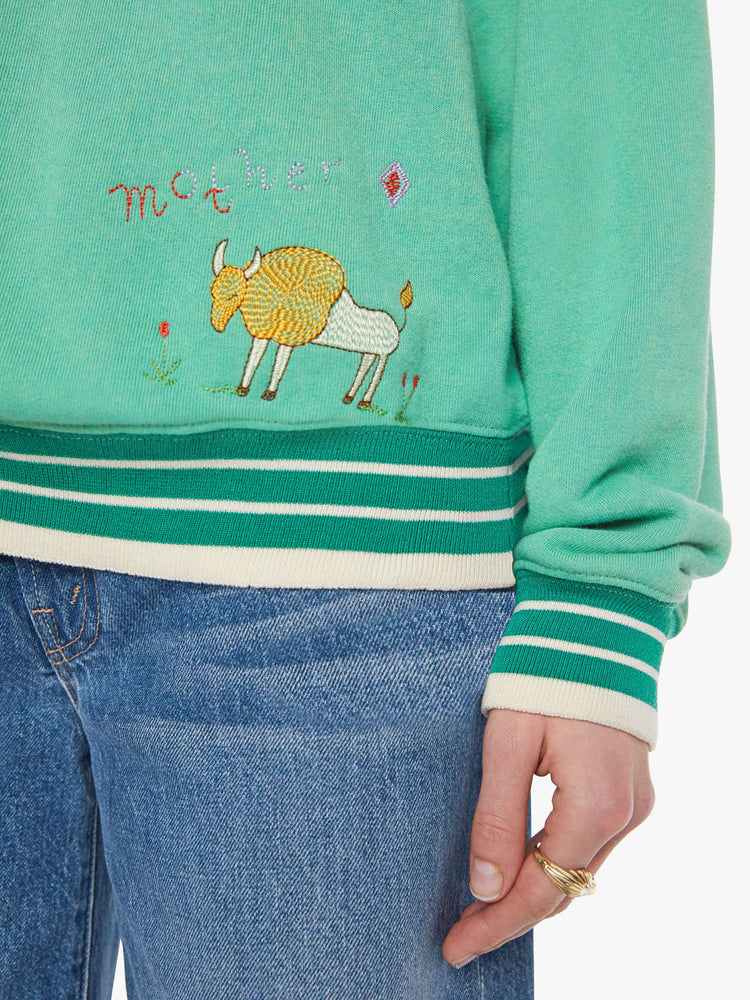 Close up view of a woman in a sun-faded green sweatshirt with colorful embroidery throughout and the number 15 appliqued on the front.
