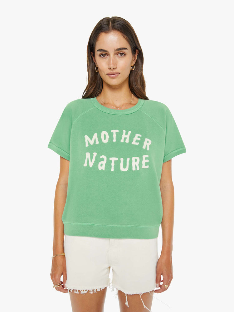 Front view of a woman in a sage green short-sleeve raglan sweatshirt with a white text graphic on the front.